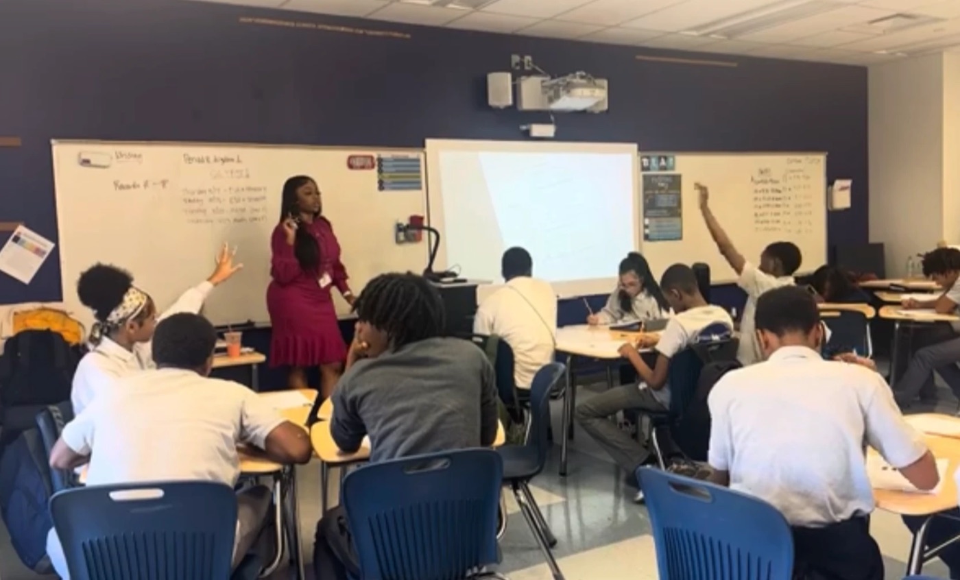 A teacher leading a classroom discussion while students raise their hands