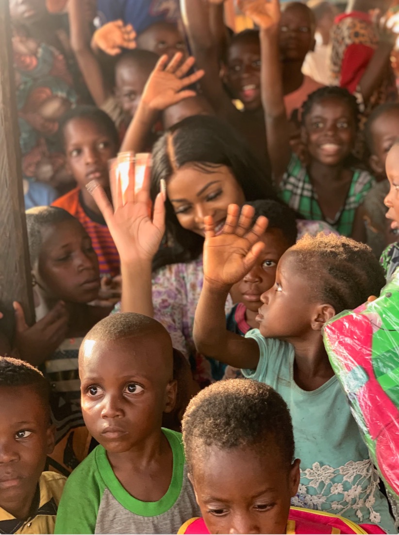 A smiling woman surrounded by children with their hands raised