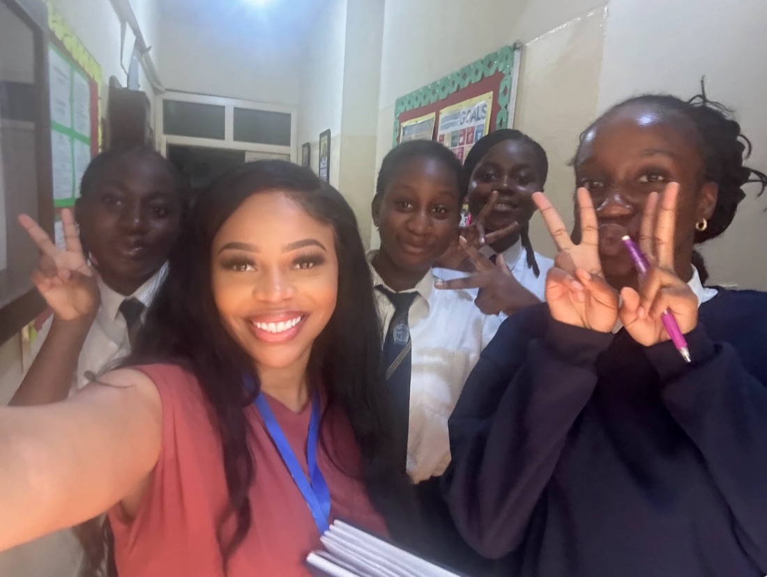 A teacher taking a selfie with four smiling students in school uniforms in a school hallway